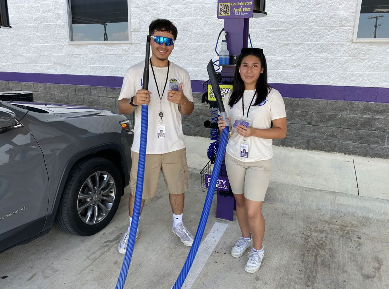 Two Feel Great Car Wash staff members showing off the complimentary vacuums and air fresheners.