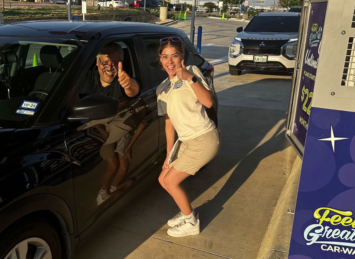 A Feel Great Car Wash employee with a satisfied customer giving two thumbs up for a great car wash.