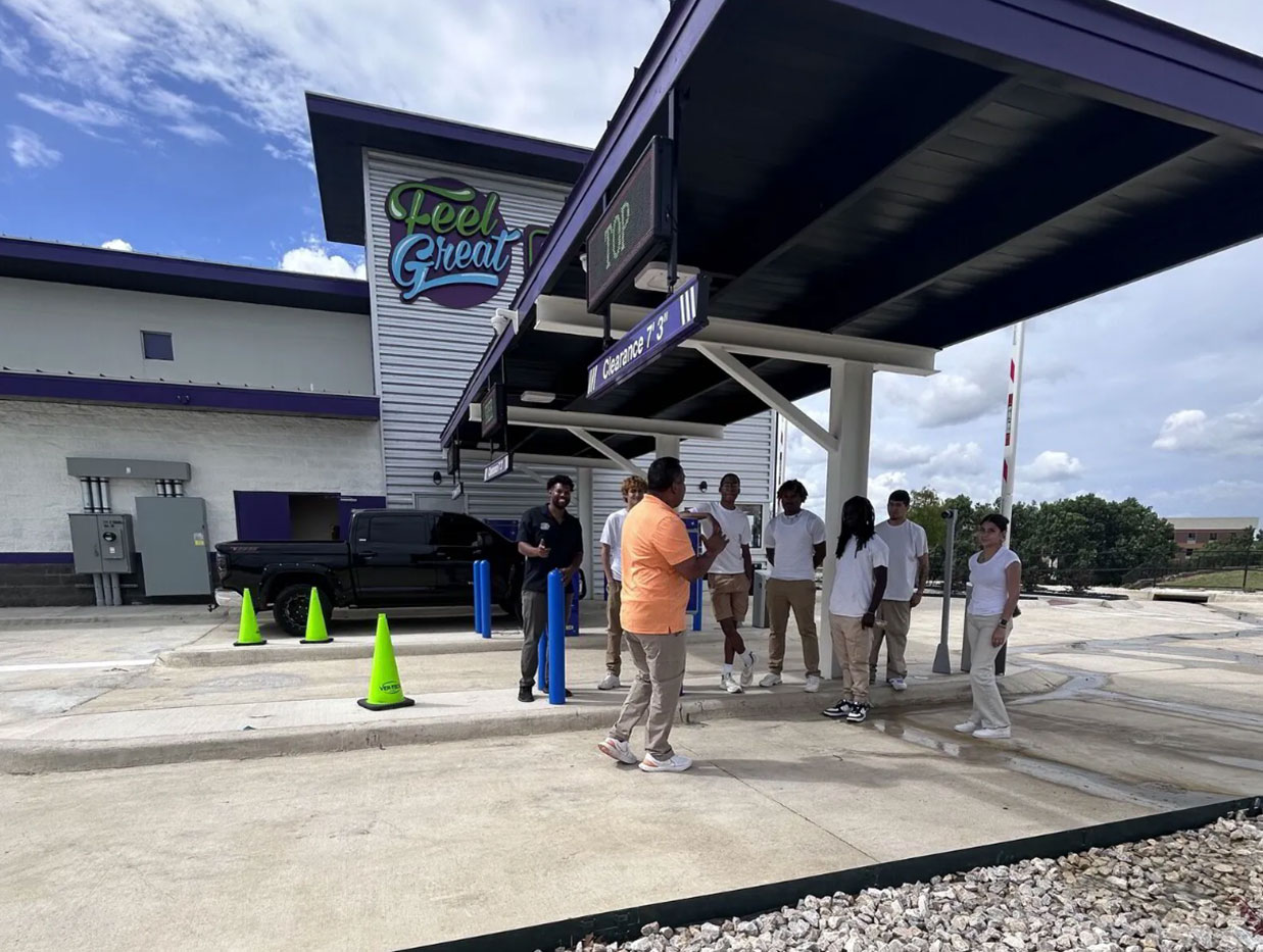 A crowd of people under a canopy at a Feel Great Car Wash location getting ready to open